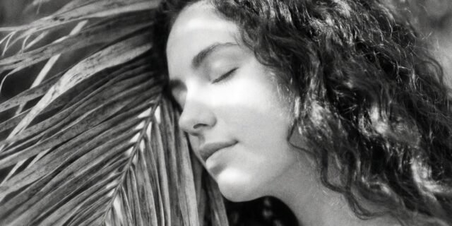 2026-01-14-Woman-With-Curly-Hair-Resting-Against-Palm-Frond-Gentle-Sleep-Serenity_19984d.jpg